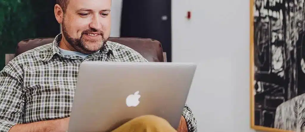 Elderly man sitting in a chair with a laptop on his lap, concentrating on online tasks