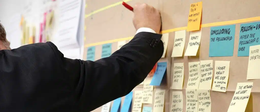 A person writing on a whiteboard filled with colorful sticky notes during a brainstorming session.