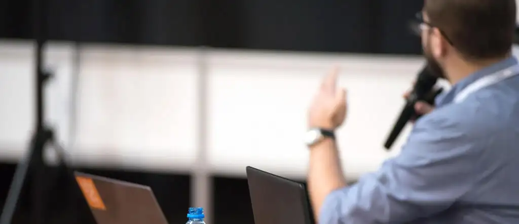 A man holding a microphone and pointing to a whiteboard, illustrating an interactive teaching session or Teaching English Online.