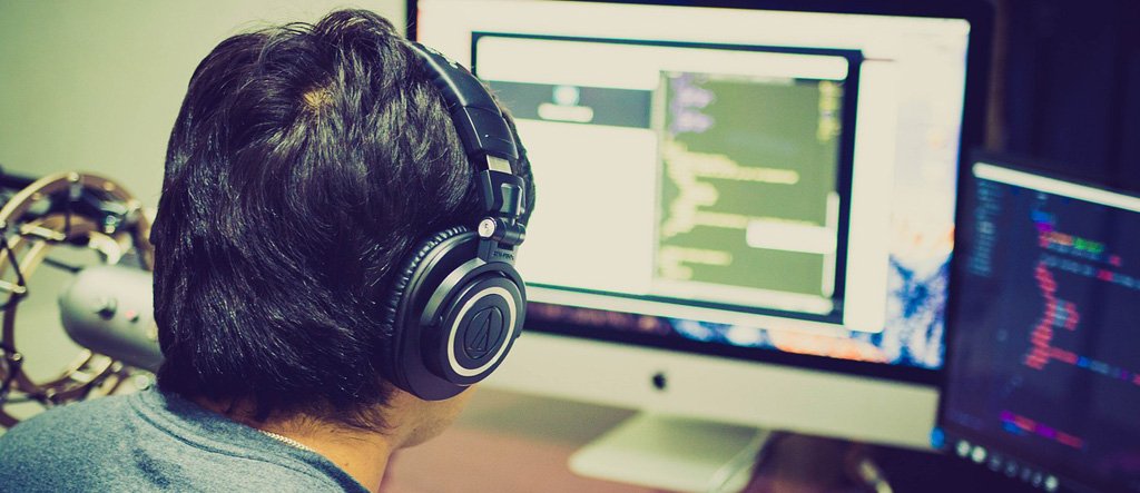 A senior man wearing headphones, working on a laptop at home, symbolizing freelance work opportunities for retirees.