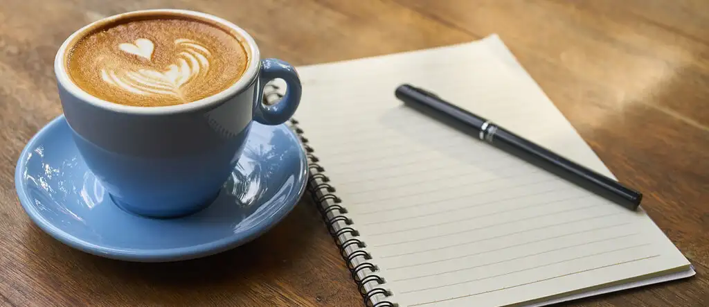 A notepad and pen beside a cup of coffee on a table, symbolizing freelance writing opportunities for seniors.