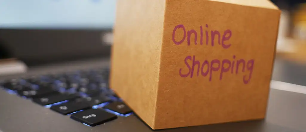 A cardboard box labeled 'Online Shopping' placed on the keyboard of a laptop, symbolizing the convenience of e-commerce and online marketplaces.