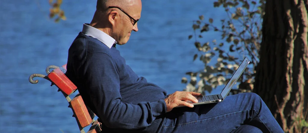 Senior man working on a laptop outside, representing staying productive while running an online business from home.