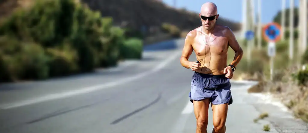 A senior man jogging along a scenic road, wearing athletic clothes and sneakers, enjoying outdoor exercise to stay fit and active.