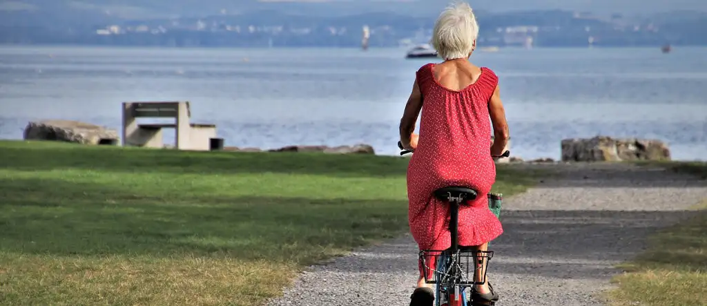 A senior woman on a bicycle, paused to admire the ocean view, symbolizing active and adventurous lifestyles in later years.