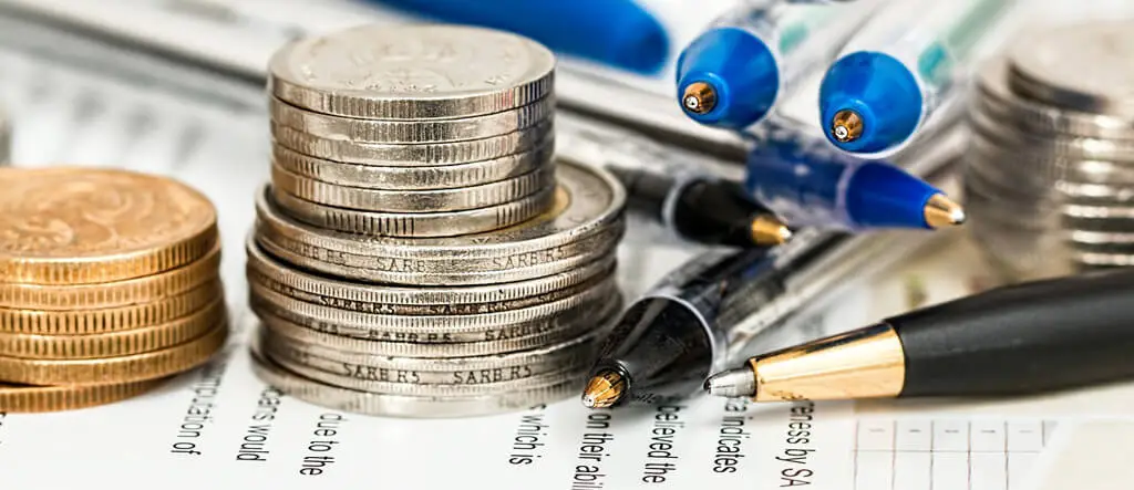 Coins, pens, and paper arranged on a desk, symbolizing low-cost business budget planning and startup strategies.