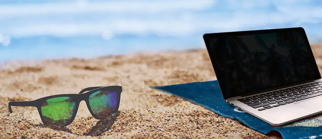 A laptop placed on sandy beach with an ocean in the background, representing the concept of working remotely from anywhere.