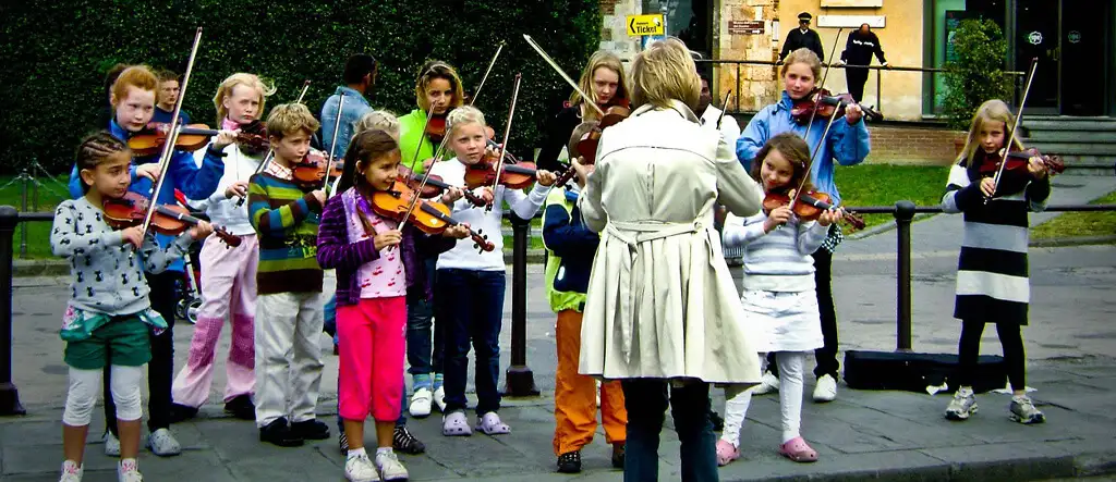 A woman conductor enthusiastically leading a children's orchestra with various instruments in a concert setting.